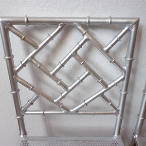 May include: Close-up of two silver metal chairs with a bamboo-style back design. The backs feature a geometric pattern with horizontal and diagonal bars, and the frames have a metallic finish. The chairs are suitable for indoor or outdoor use.