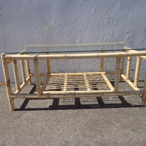 May include: A light brown bamboo coffee table with a glass top and a lower shelf. The table has a simple, rectangular design with a woven bamboo base.