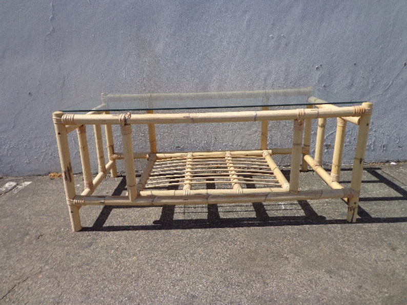 May include: A light brown bamboo coffee table with a glass top and a lower shelf. The table has a simple, rectangular design with a woven bamboo base.