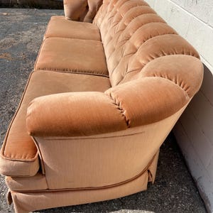 May include: A light brown tufted sofa with a curved back and rolled arms. The sofa is upholstered in a soft, velvety fabric.