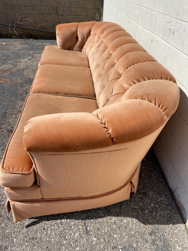 May include: A light brown tufted sofa with a curved back and rolled arms. The sofa is upholstered in a soft, velvety fabric.