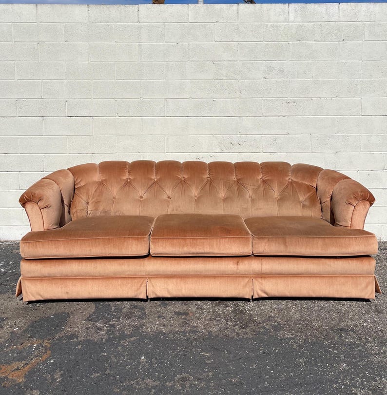 May include: A vintage tufted sofa upholstered in a soft peach-colored velvet fabric. The sofa has a classic design with rolled arms and a button-tufted back.