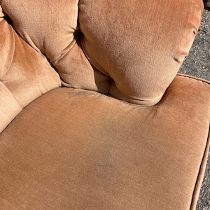 May include: A close-up of a brown velvet armchair with tufted upholstery. The fabric has a subtle sheen and a slightly worn appearance.