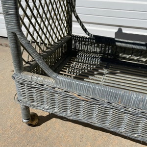 May include: A gray wicker chaise lounge with brass wheels. The chaise lounge has a woven wicker design and is in good condition.