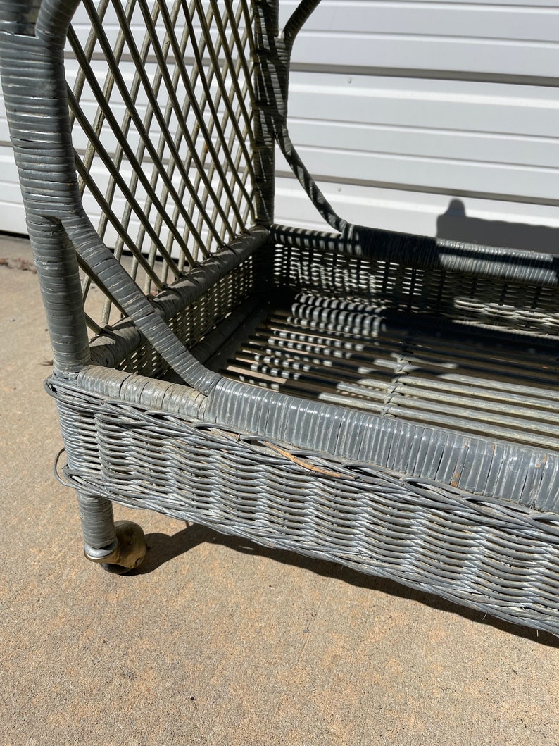 May include: A gray wicker chaise lounge with brass wheels. The chaise lounge has a woven wicker design and is in good condition.