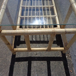 May include: A rectangular bamboo coffee table with a glass top. The table has a natural wood finish and is made of woven bamboo.