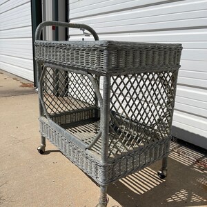 May include: A gray wicker serving cart with two shelves and four wheels. The cart has a woven design and is in good condition.
