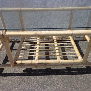 May include: A rectangular bamboo coffee table with a glass top and a lower shelf. The table is made of natural bamboo and has a light brown color.