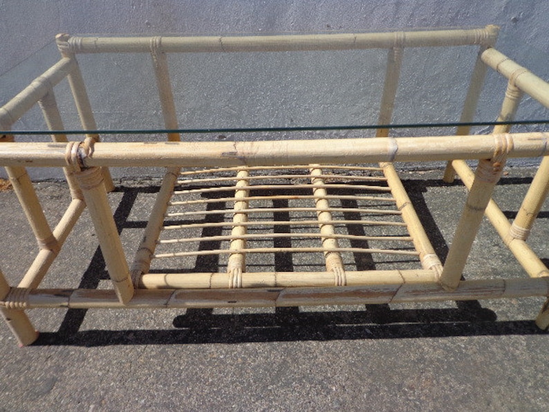 May include: A rectangular bamboo coffee table with a glass top and a lower shelf. The table is made of natural bamboo and has a light brown color.