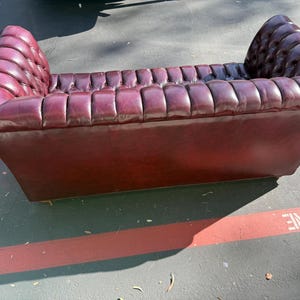 May include: A burgundy leather loveseat with a tufted design. The sofa has a low profile with a rectangular base and gently curved armrests. The seat and back are deeply tufted, adding texture and visual interest. The piece is designed for seating.