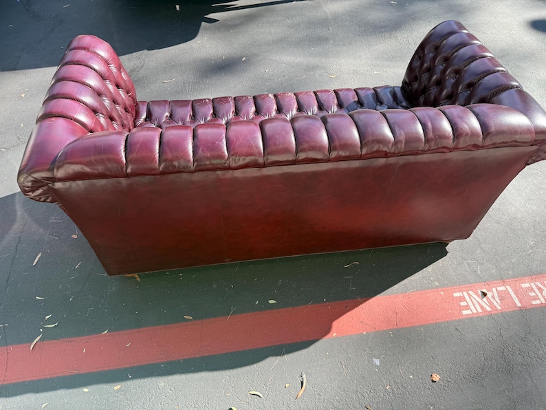 May include: A burgundy leather loveseat with a tufted design. The sofa has a low profile with a rectangular base and gently curved armrests. The seat and back are deeply tufted, adding texture and visual interest. The piece is designed for seating.