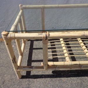 May include: A natural bamboo coffee table with a glass top and a woven bamboo shelf. The table has a light brown color and a simple design.