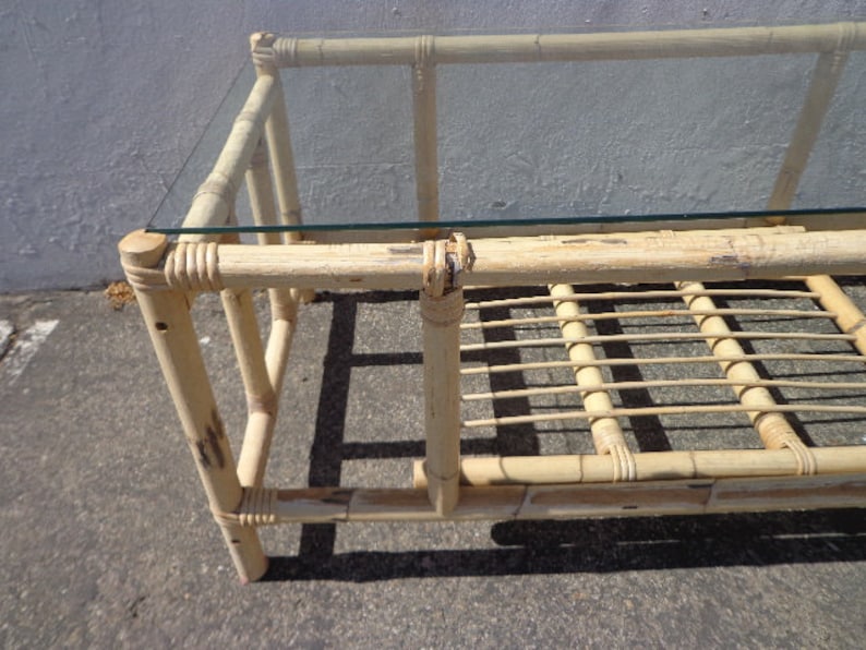May include: A natural bamboo coffee table with a glass top and a woven bamboo shelf. The table has a light brown color and a simple design.