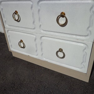 May include: White dresser with four drawers and gold ring pulls. The dresser has a beige base.
