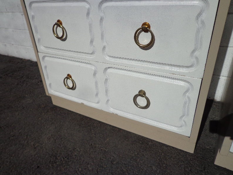 May include: White dresser with four drawers and gold ring pulls. The dresser has a beige base.