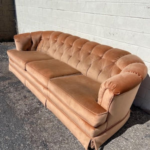 May include: A long, tufted, peach-colored velvet sofa with rolled arms and a button-tufted back.