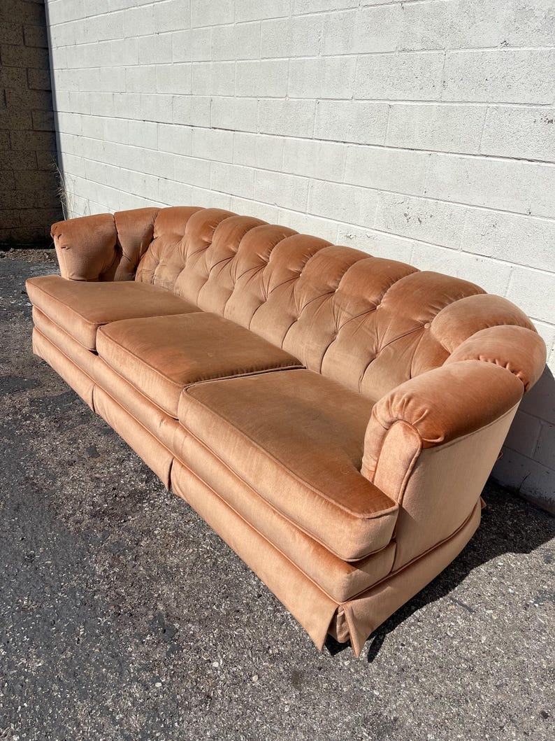 May include: A long, tufted, peach-colored velvet sofa with rolled arms and a button-tufted back.