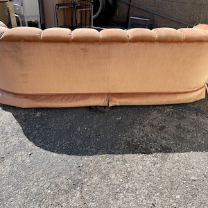 May include: A peach-colored tufted sofa with a curved back and a slightly rounded front. The sofa has a light brown fabric upholstery and a decorative trim around the bottom.