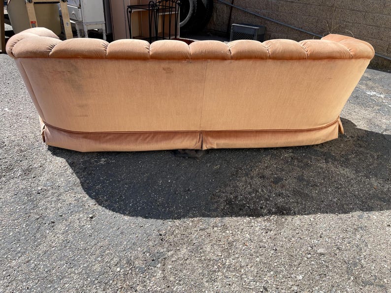 May include: A peach-colored tufted sofa with a curved back and a slightly rounded front. The sofa has a light brown fabric upholstery and a decorative trim around the bottom.