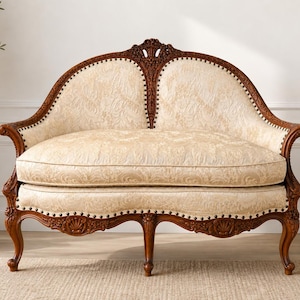 May include: A two-seater loveseat featuring a dark brown carved wooden frame with intricate floral detailing and a cream-colored upholstered seat and backrest with a subtle damask pattern, supported by curved cabriole legs with nailhead trim.