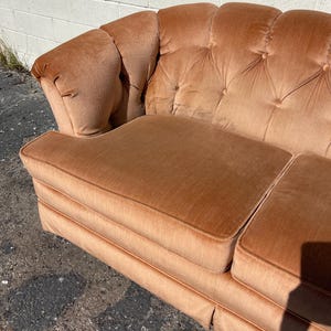 May include: A vintage tufted sofa upholstered in a peachy-orange velvet fabric. The sofa has a classic design with a rounded back and arms.