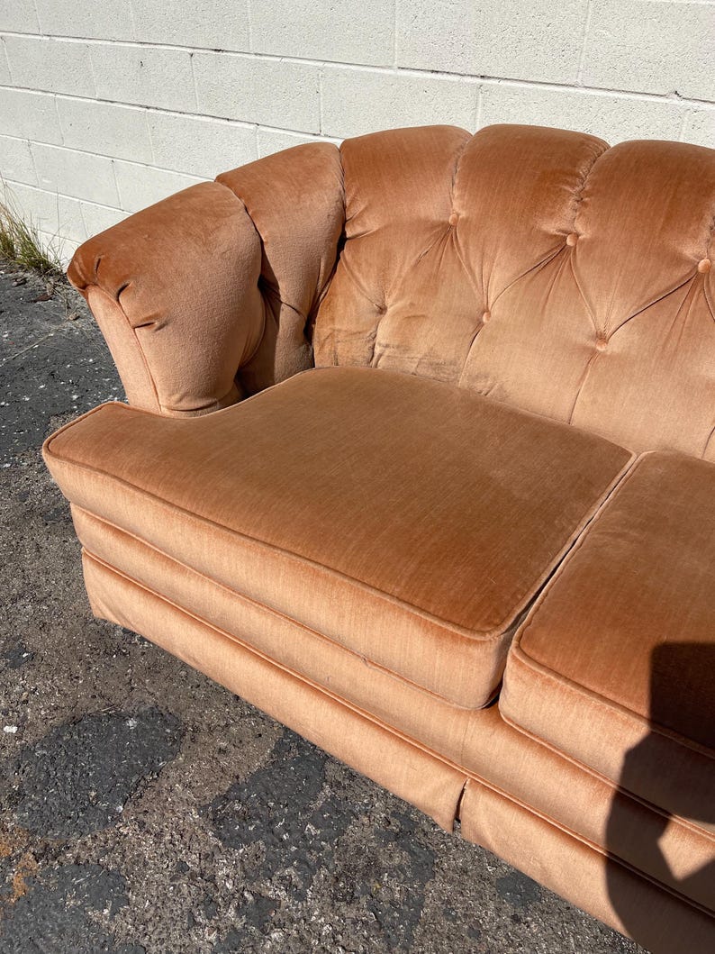 May include: A vintage tufted sofa upholstered in a peachy-orange velvet fabric. The sofa has a classic design with a rounded back and arms.