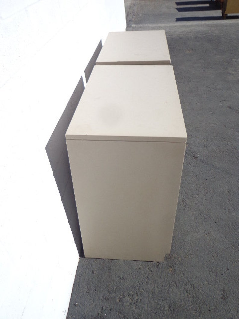 May include: Two off-white, rectangular, wooden nightstands with drawers. The nightstands are stacked on top of each other.