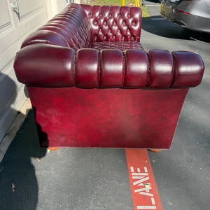 May include: A burgundy leather Chesterfield sofa with a tufted back and rolled arms. The sofa has a low profile and is set on wooden feet. The sofa is a classic piece of furniture.