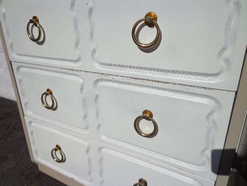 May include: White dresser with four drawers and gold ring-shaped handles. The dresser has a decorative, scalloped edge.