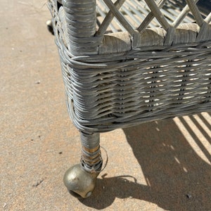 May include: A gray wicker rolling cart with a metal frame and wheels. The cart has a woven design and is made of natural materials.