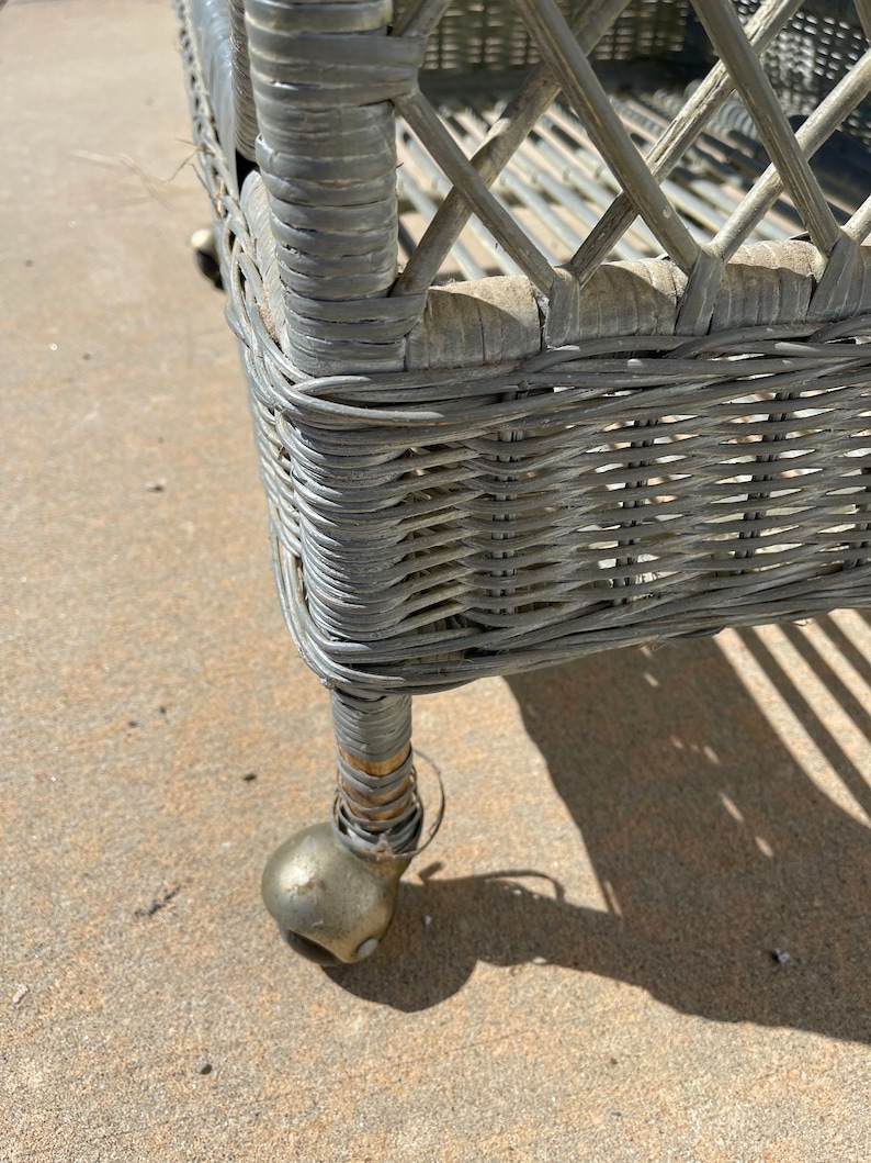 May include: A gray wicker rolling cart with a metal frame and wheels. The cart has a woven design and is made of natural materials.
