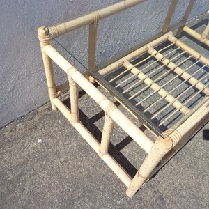 May include: A light brown bamboo coffee table with a glass top. The table has a rectangular shape and a simple design.