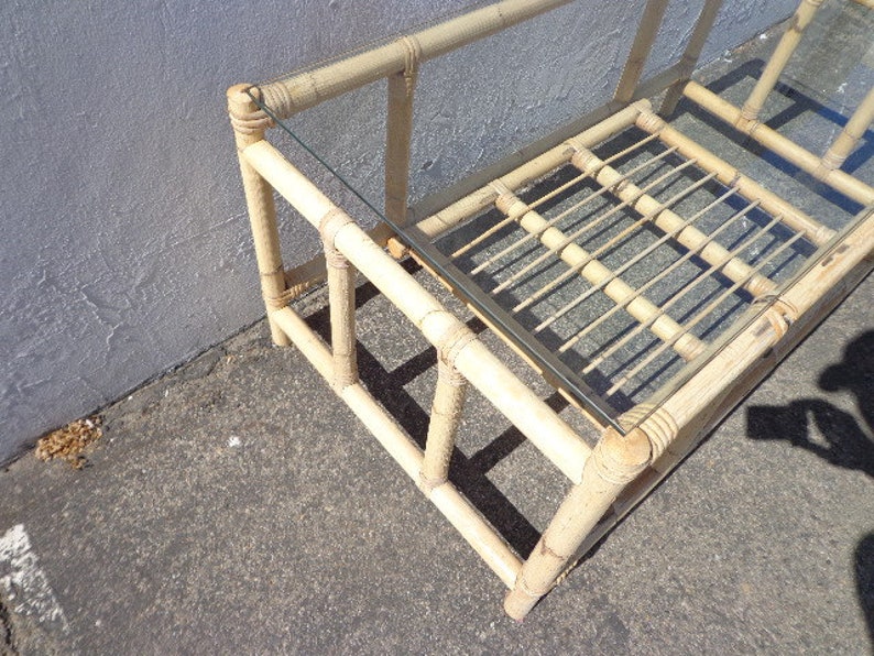 May include: A light brown bamboo coffee table with a glass top. The table has a rectangular shape and a simple design.
