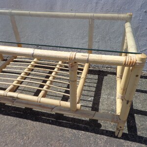 May include: A light brown bamboo coffee table with a glass top and a lower shelf. The table has a simple, rectangular design and is made of natural materials.