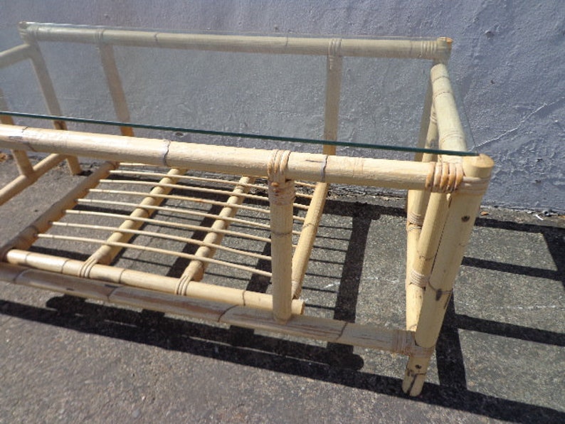 May include: A light brown bamboo coffee table with a glass top and a lower shelf. The table has a simple, rectangular design and is made of natural materials.