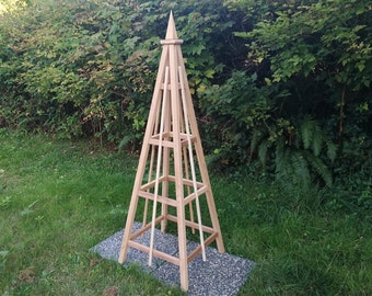 May include: A wooden pyramid-shaped garden trellis with a pointed top and four vertical supports. The trellis is made of natural wood and has a rustic look.