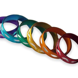 May include: Six colorful metal rings with a white design. The rings are arranged in a rainbow pattern, starting with purple and ending with red.