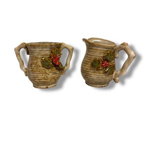 May include: A set of two ceramic salt and pepper shakers with a brown and white striped design. The shakers have a holly leaf and berry design on the front.