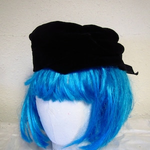 May include: A black velvet hat with a slightly rounded crown and a wide brim. The hat is sitting on a mannequin head with bright blue hair.