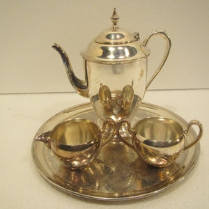 May include: A silver tea set with a teapot, creamer, and sugar bowl on a silver tray. The set has an ornate design.