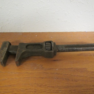 May include: A vintage adjustable wrench with a black metal finish. The wrench has a long handle and a jaw that can be adjusted to fit different sizes of nuts and bolts.