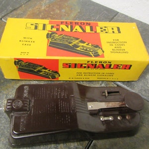 May include: A brown plastic device labeled "FLERON SIGNALER" with instructions for using codes and blinker signaling. The device is in its original box, which is yellow with red and black lettering.