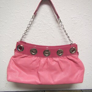May include: A pink perforated leather handbag with a silver chain strap and silver grommets around the top.