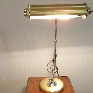 May include: A gold-toned desk lamp with a long, adjustable arm and a rectangular shade. The lamp is on a wooden table.