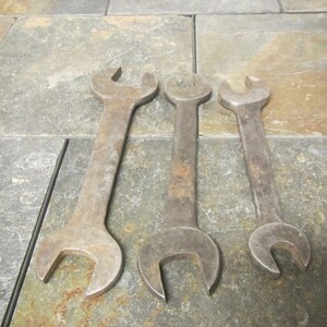 May include: Three vintage metal wrenches of different sizes, laid out on a slate tile surface.