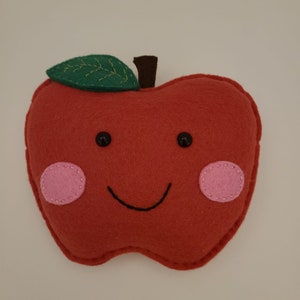 May include: A red felt apple with a green felt leaf, black eyes, a stitched smile, and pink felt cheeks.
