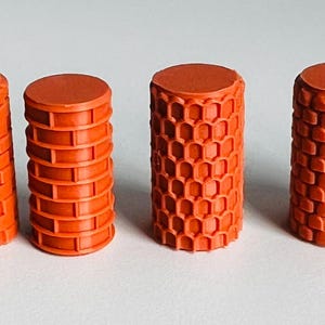 May include: Six orange cylindrical objects with varying textured surfaces. The textures include diamond patterns, brick-like designs, and honeycomb shapes. Each cylinder has a flat top and bottom, and they are arranged in a row.