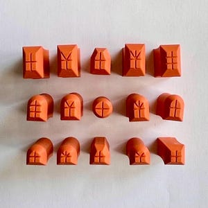 May include: Orange architectural building blocks in various shapes, including rectangular, arched, and rounded forms. Each block features a cross or window design, suitable for construction or educational play.