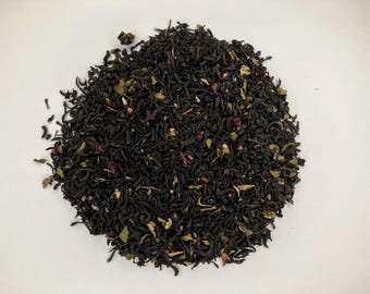 May include: A close-up of a blend of black tea leaves, dried fruit pieces, and herbs. The tea leaves are dark brown and black, and the fruit pieces are red and white.