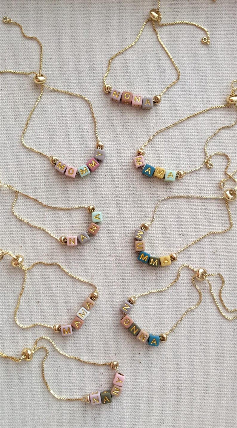 May include: A set of nine gold chain bracelets with colorful beads spelling out different names. The names include MOMMY, ZAMA, NANA, MUMMA, MAMA, ANNA, NONA, and ONNA.